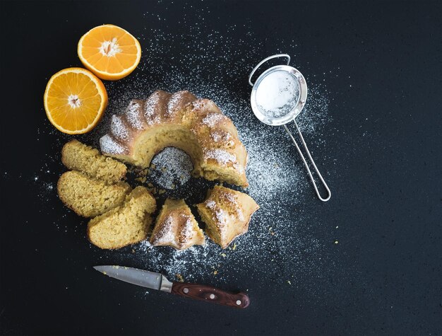 Pastel húmedo de yogur de naranja con polvo de azúcar en la parte superior del fondo oscuro del grunge