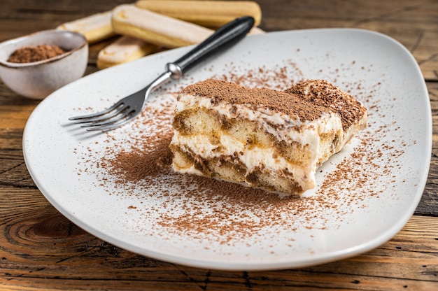 Pastel italiano de tiramisú con cacao en un plato. Fondo de madera. Vista superior.