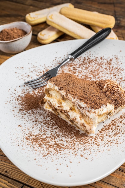 Pastel italiano de tiramisú con cacao en un plato. Fondo de madera. Vista superior.