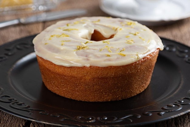 Pastel de limón redondo casero con cobertura y ralladura de limón en un plato sobre una mesa rústica de madera