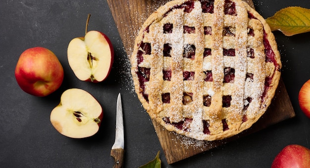 Pastel de manzana tradicional redondo horneado sobre tablero de madera marrón y manzanas rojas frescas, vista superior