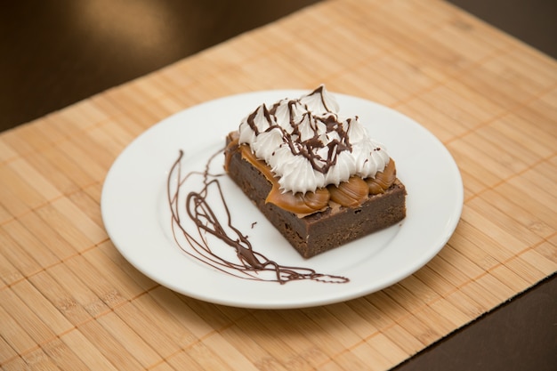 Pastel de marquesa Pastel de chocolate estilo brownie cubierto con una capa de dulce de leche y otra capa de merengue. En plato blanco sobre alfombra de madera