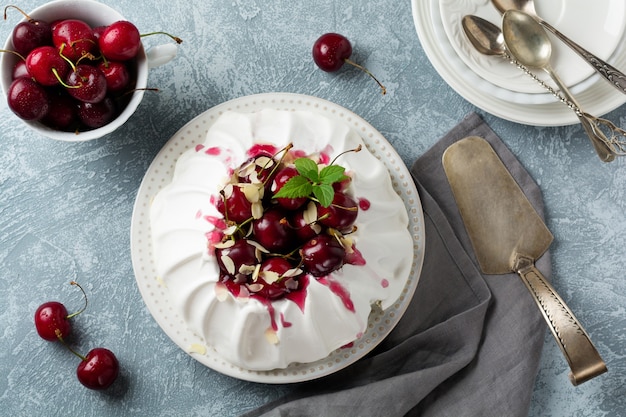 Pastel de merengue casero Pavlova con crema batida, cereza fresca y salsa sobre hormigón ligero