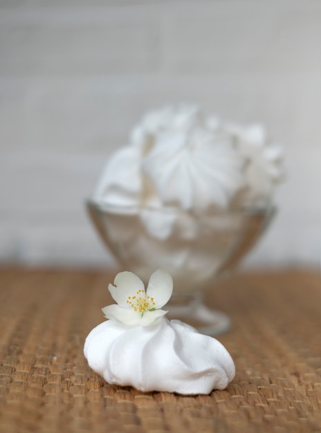 Pastel de merengue, en un jarrón de vidrio con una flor de jazmín sobre un fondo de mimbre