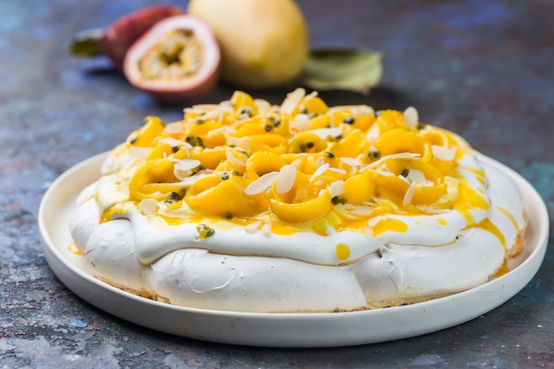 Pastel de merengue Pavlova con mango fresco y maracuyá y crema batida sobre fondo de pizarra, piedra u hormigón