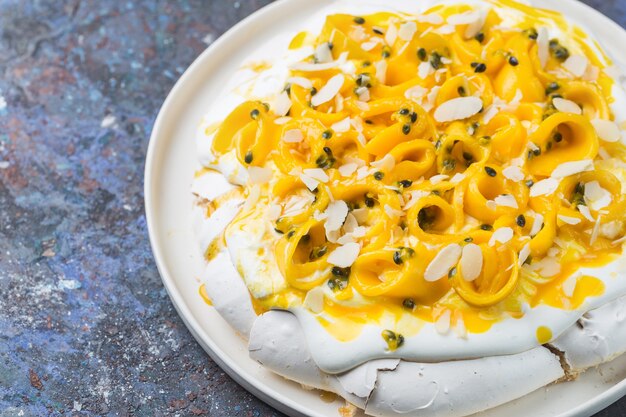 Pastel de merengue Pavlova con mango fresco y maracuyá y crema batida sobre fondo de pizarra, piedra u hormigón