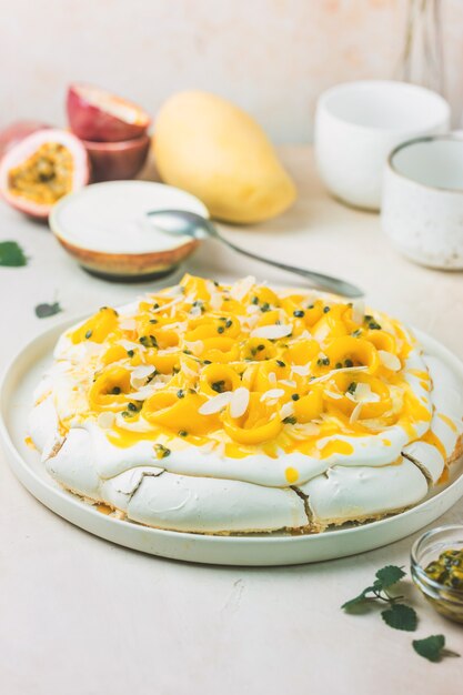 Pastel de merengue Pavlova con mango fresco y maracuyá y crema batida sobre fondo de pizarra, piedra u hormigón