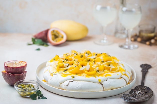 Pastel de merengue Pavlova con mango fresco y maracuyá y crema batida sobre fondo de pizarra, piedra u hormigón