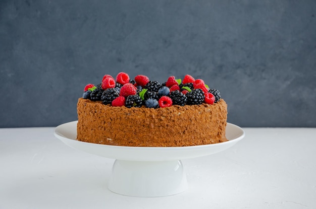 Pastel de miel de chocolate con crema y bayas frescas en la parte superior sobre una placa blanca sobre un fondo de hormigón