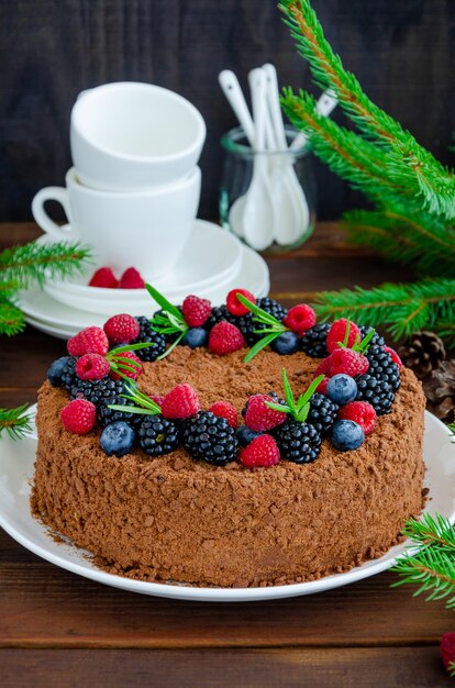 Pastel de miel de chocolate con crema y bayas frescas en la parte superior sobre un plato blanco sobre una mesa de madera.