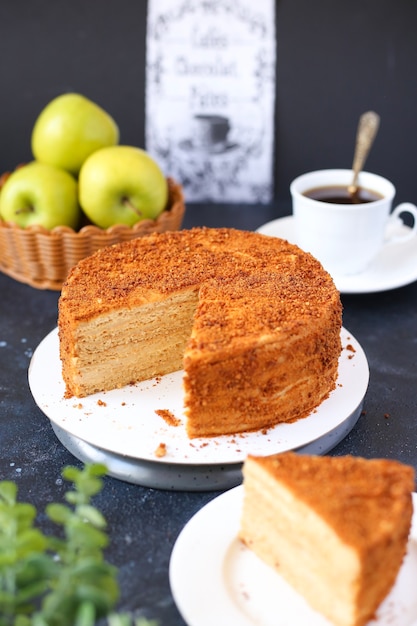 Pastel de miel sobre fondo oscuro con manzanas verdes, café y flores.