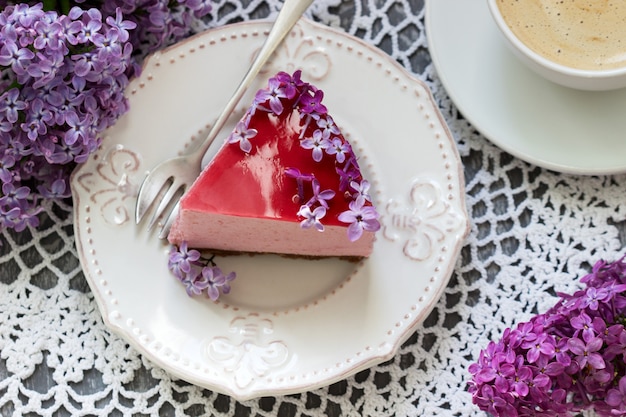 Un pastel de mousse de bayas con base de chocolate y gelatina de jugo, decorado con flores lilas, servido con café.