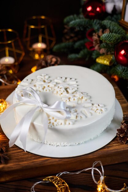 Pastel de mousse blanco navideño decorado con copos de nieve y un lazo sobre el fondo de velas