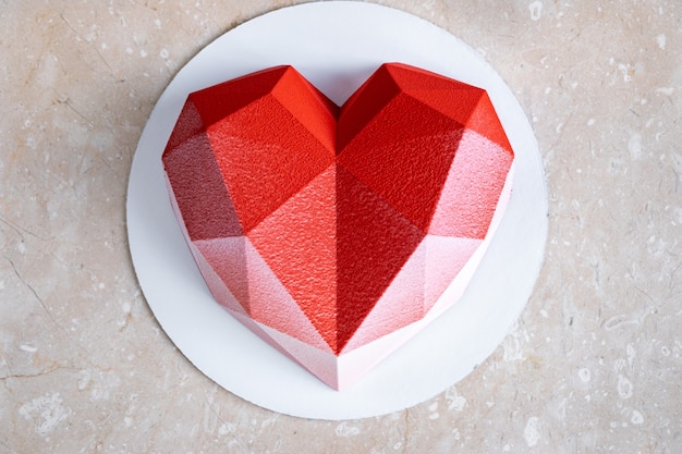 Foto pastel de mousse de corazón rojo facetado con revestimiento de terciopelo sobre una mesa de mármol rosa suave.