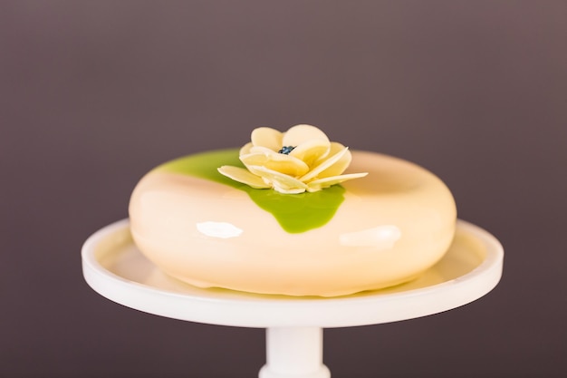 Pastel de mousse gourmet con glaseado espejo blanco y verde decorado con flor de chocolate blanco.