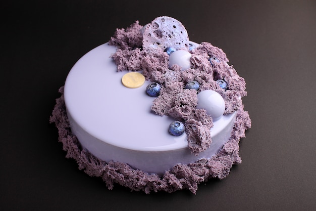 Pastel con mousse de moras en el esmalte de espejo decorado con una galleta molecular. Sobre el fondo negro.