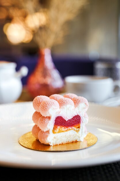 Un pastel de mousse rosa con gelatina de frambuesa y relleno de plátano en una placa blanca en un restaurante, primer plano vertical