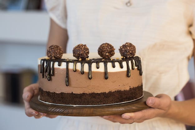 Pastel de mousse "tres chocolates". Pedazo de pastel hecho de tres capas de chocolate de soufflé de diferentes colores en mano de mujer