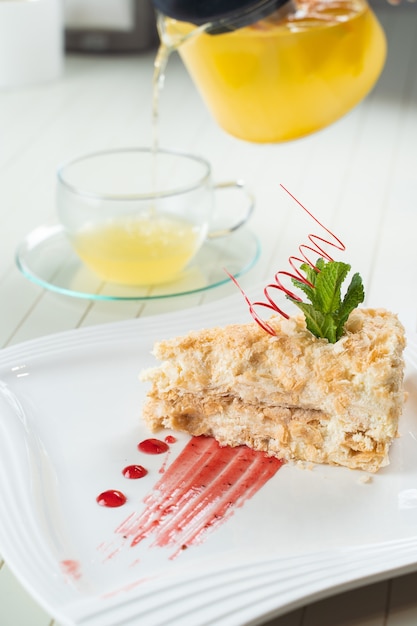 Pastel de Napoleón decorado con una espiral de chocolate rojo, menta y mermelada de bayas en una placa blanca.