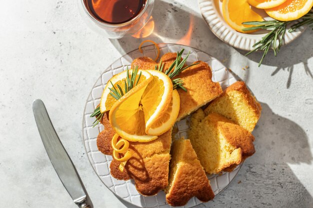 Pastel de naranja esponjoso en rodajas decorado con rodajas de naranja frescas sobre cerámica sobre fondo de textura gris claro desayuno matutino soleado con luz dura Espacio de texto plano vista superior