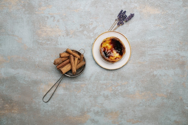 Pastel de nata. Postre tradicional portugués, tarta de huevo en el plato sobre fondo rústico con ramas de canela en el colador y ramitas de lavanda secas. Vista superior