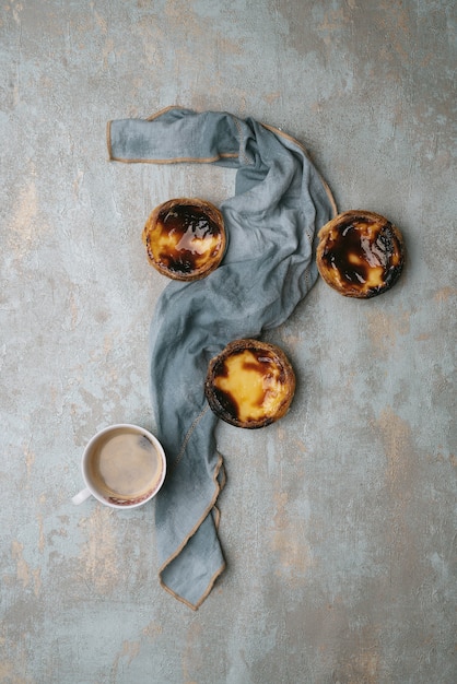 Pastel de nata. Postre tradicional portugués, tartas de huevo sobre fondo rústico y taza de café decorada con servilleta. Vista superior