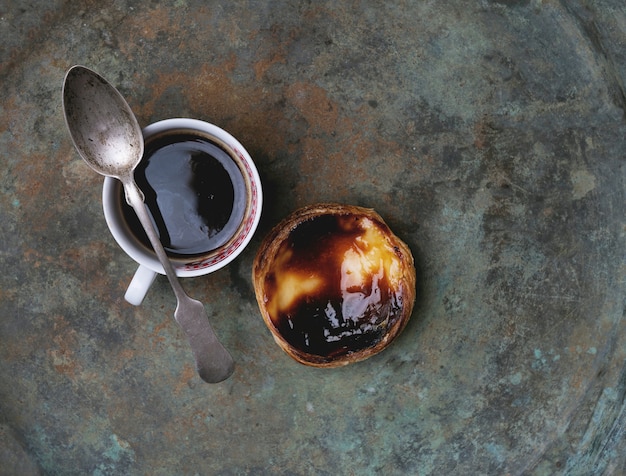 Pastel de nata. Tarta de huevo de postre tradicional portuguesa y taza de café sobre fondo de metal rústico. Vista superior