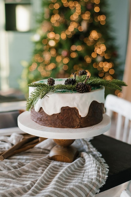 El pastel de Navidad festivo con helado blanco decorado con ramas de abeto se encuentra en una mesa puesta contra un fondo de luces