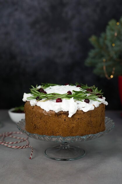 Pastel de Navidad con romero y bayas rojas en un stand sobre un fondo gris y negro