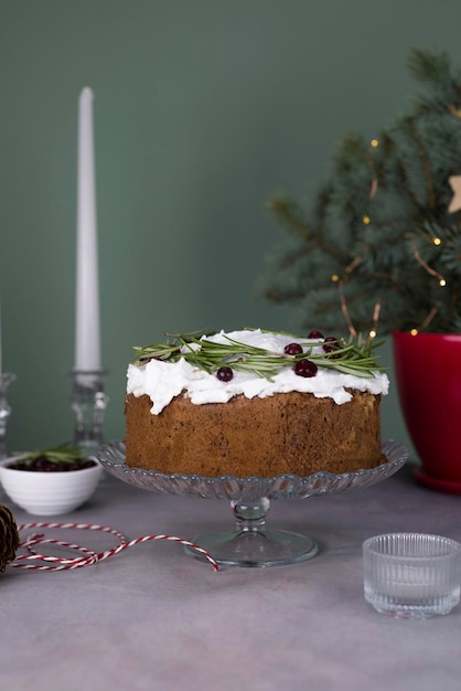 Pastel de Navidad con romero y bayas rojas en un stand sobre un fondo gris y verde