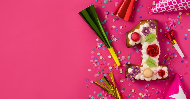 Pastel número uno decorado con flores y galletas en la vista panorámica de superficie rosa