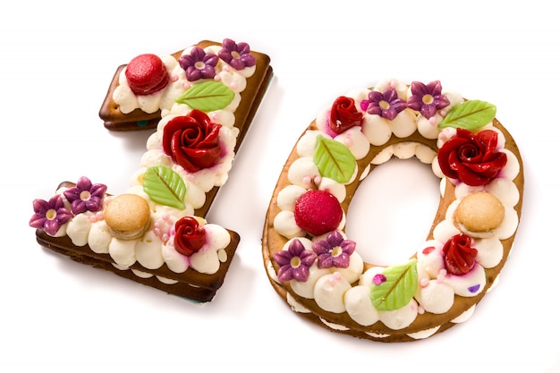 Pastel número diez decorado con flores y macarons aislados en superficie blanca.