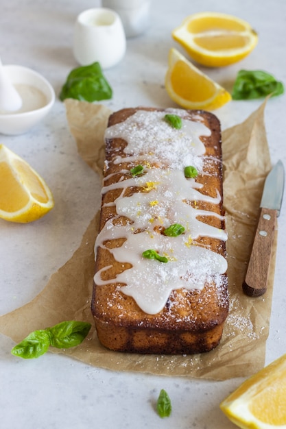 Pastel de pan de limón glaseado casero decorado con ralladura de limón, albahaca y chips de coco.