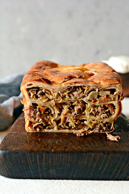 Pastel de panqueques con carne y champiñones sobre un fondo gris. Torta de panqueques en forma de pan.