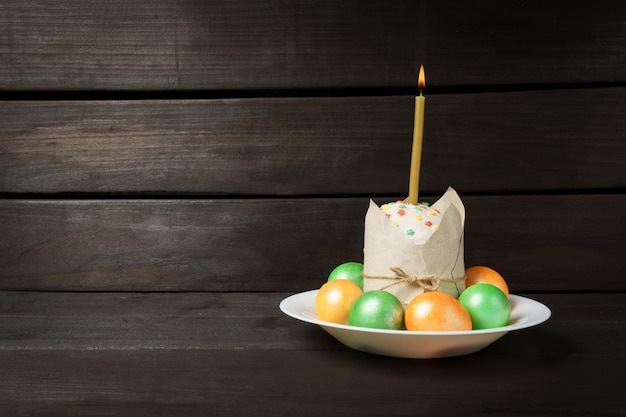 Pastel de Pascua con huevos pintados de colores sobre una mesa oscura, se quema una vela de la iglesia insertada en el pastel