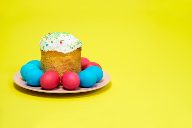 Pastel de Pascua y huevos pintados sobre un fondo amarillo.