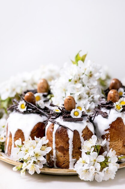 Pastel de Pascua tradicional casero con nidos de chocolate y huevos en plato de cerámica y cerezo floreciente sobre fondo blanco Tradicional ortodoxo Pascua Ruso Ucraniano hornear Cerrar