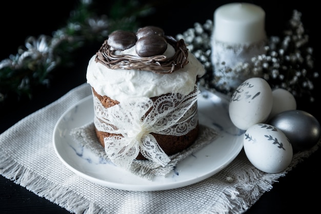 Pastel de Pascua tradicional con huevos pintados de plata, velas y sauce sobre una superficie negra. Enfoque selectivo