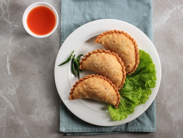 Pastel de pastel indonesio servido en un plato blanco acompañado de té. Popular como Curry Puff (Karipap) o Jalangkote Makasar.