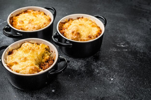 Pastel de pastor casero con carne molida, puré de papa y costra de queso cheddar. Fondo negro. Vista superior. Copie el espacio.