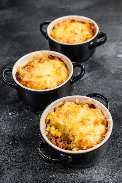 Pastel de pastor casero con carne molida, puré de papa y costra de queso cheddar. Fondo negro. Vista superior.