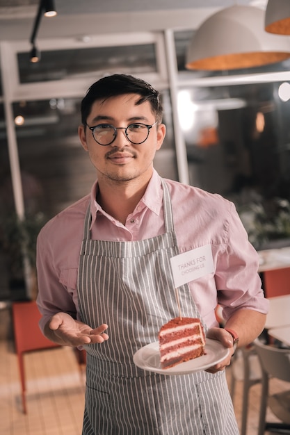 Pastel en un plato. Joven empresario prometedor inteligente sosteniendo un delicioso pastel en un plato blanco forma su café