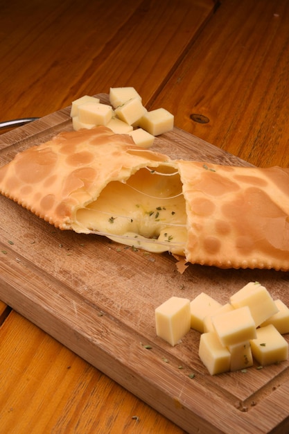 Foto pastel de queso cortado con queso derretido cayendo sobre una tabla y cubos de queso