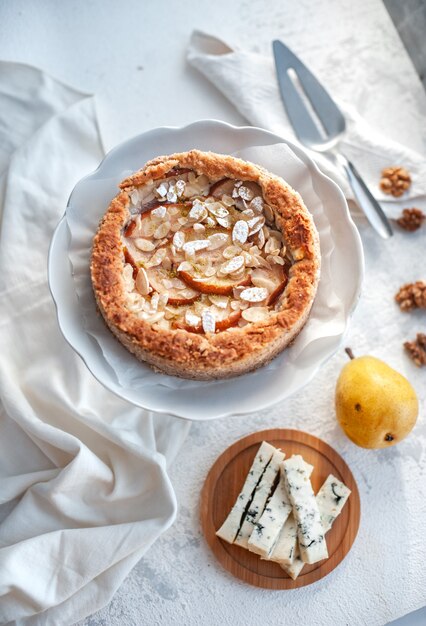 Foto pastel con queso dor azul, peras y almendras, todo redondo en un plato sobre una mesa blanca.