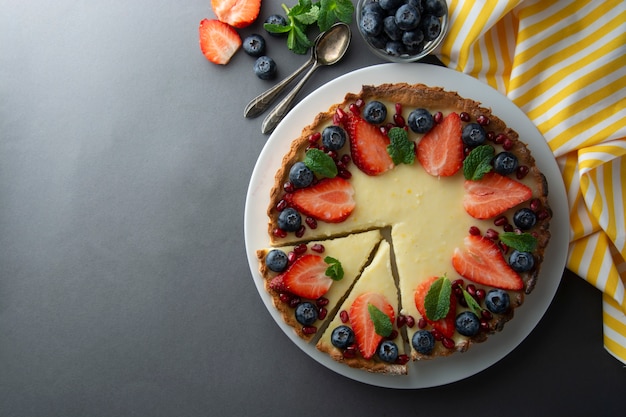 Pastel de queso entero con bayas frescas y menta para el postre. Fondo gris