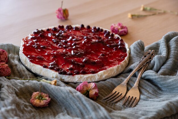 Foto pastel de queso frío con jalea de cereza y rosas a su alrededor servido sobre fondo de madera con lanza verde y tenedores antiguos