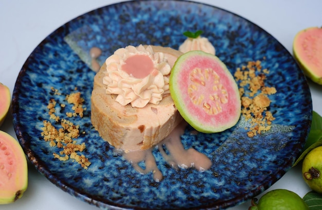 Pastel de rollo de guayaba en plato azul sobre fondo claro con fruta de guayaba madura