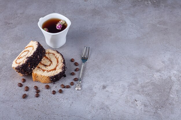 Pastel de rollo en rodajas con granos de café y una taza de té sobre fondo de piedra.