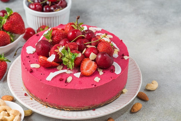 Un pastel rosa con cerezas y almendras encima.