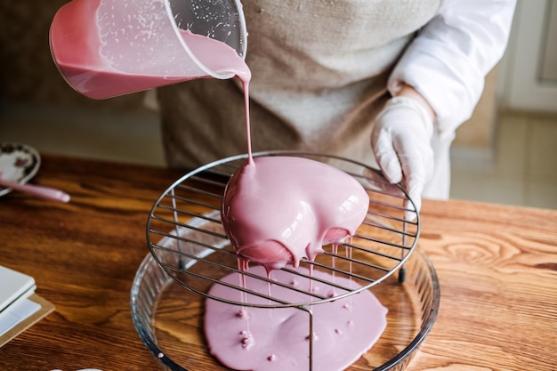 Pastel rosa con forma de corazón de mousse en la mano de una mujer árabe asiática pastelera proceso de pastel de glaseado de espejo